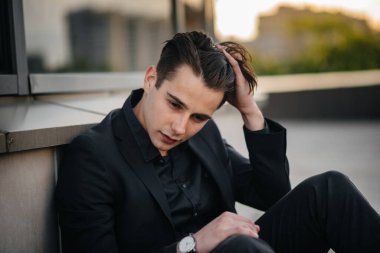 Şık bir genç adam gün batımında aynalı bir binanın yanında duruyor. Moda.