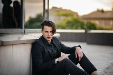 Şık bir genç adam gün batımında aynalı bir binanın yanında duruyor. Moda.