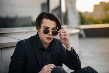 Şık bir genç adam gün batımında aynalı bir binanın yanında duruyor. Moda.