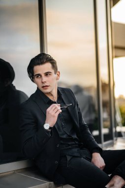 Şık bir genç adam gün batımında aynalı bir binanın yanında duruyor. Moda.