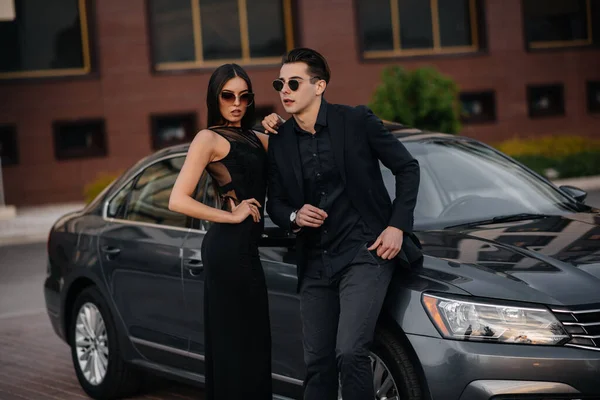 日没時に車の近くに黒の若いスタイリッシュなカップルが立っている ファッション スタイル — ストック写真