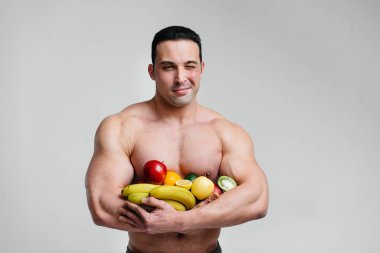 Parlak meyveli beyaz bir arka planda poz veren sportif seksi adam. Diyet olsun. Sağlıklı beslenme