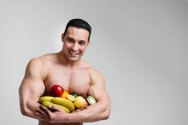 Parlak meyveli beyaz bir arka planda poz veren sportif seksi adam. Diyet olsun. Sağlıklı beslenme