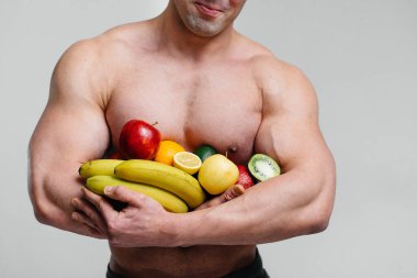 Parlak meyveli beyaz bir arka planda poz veren sportif seksi adam. Diyet olsun. Sağlıklı beslenme