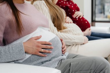 Hamile kızlar göbeklerini elleriyle yakın plan çekimde tutarlar. Hamile kızların doğum öncesi sınıfı.