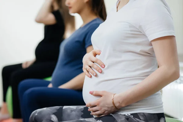 Bir grup hamile anne bir fitness kulübünde pilates ve top sporu yapıyor. Karnı yakın çekim.