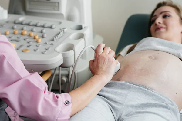 Stock image A pregnant girl is having an ultrasound of the abdomen in the clinic in close-up. Medical examination