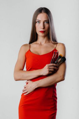 Güzel genç bir makyöz, Stüdyoda beyaz bir arka planda püskülleriyle poz veriyor. Makyaj