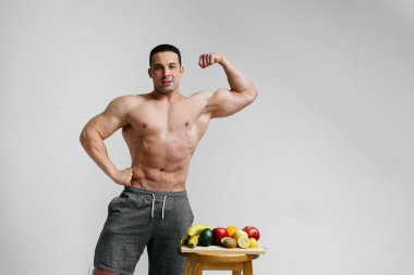 Parlak meyveli beyaz bir arka planda poz veren sportif seksi adam. Diyet olsun. Sağlıklı beslenme