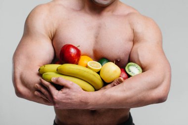 Parlak meyveli beyaz bir arka planda poz veren sportif seksi adam. Diyet olsun. Sağlıklı beslenme