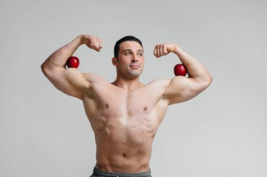 Parlak meyveli beyaz bir arka planda poz veren sportif seksi adam. Diyet olsun. Sağlıklı beslenme