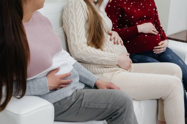 Hamile kızlar göbeklerini elleriyle yakın plan çekimde tutarlar. Hamile kızların doğum öncesi sınıfı.