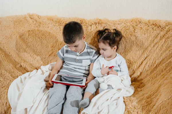 Brother and sister play on the couch in the tablet