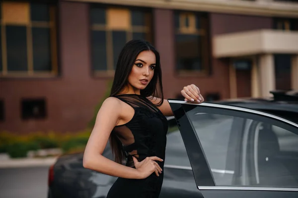 身穿黑色连衣裙的时髦少女站在汽车旁边 商务时尚和风格 — 图库照片