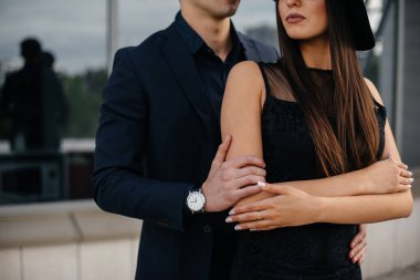 Siyah elbiseli ve gözlüklü güzel, şık bir çift genç gün batımında bir ofis binasının arka planında duruyor. Moda ve tarz