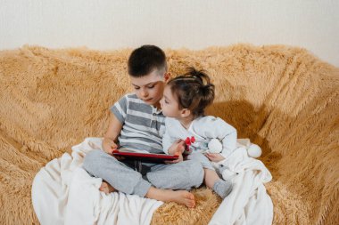 Erkek ve kız kardeş tabletteki kanepede oynuyorlar.
