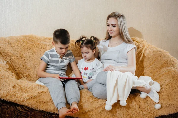 美しいです妊娠中のお母さん座っていますザソファとともに彼女の息子と娘とプレイタブレット — ストック写真