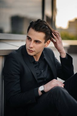 Şık bir genç adam gün batımında aynalı bir binanın yanında duruyor. Moda.