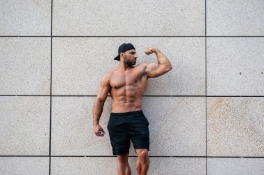 Seksi sporcu duvarın yanında üstsüz duruyor. Fitness, vücut geliştirme