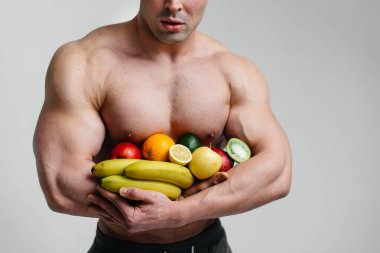 Parlak meyveli beyaz bir arka planda poz veren sportif seksi adam. Diyet olsun. Sağlıklı beslenme