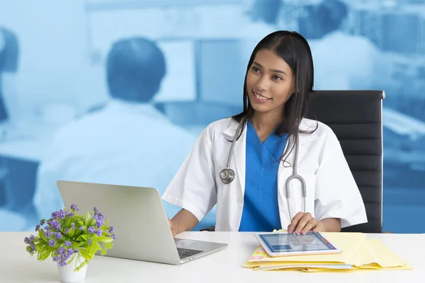 Female doctor smiled welcome while working on a notebook and com