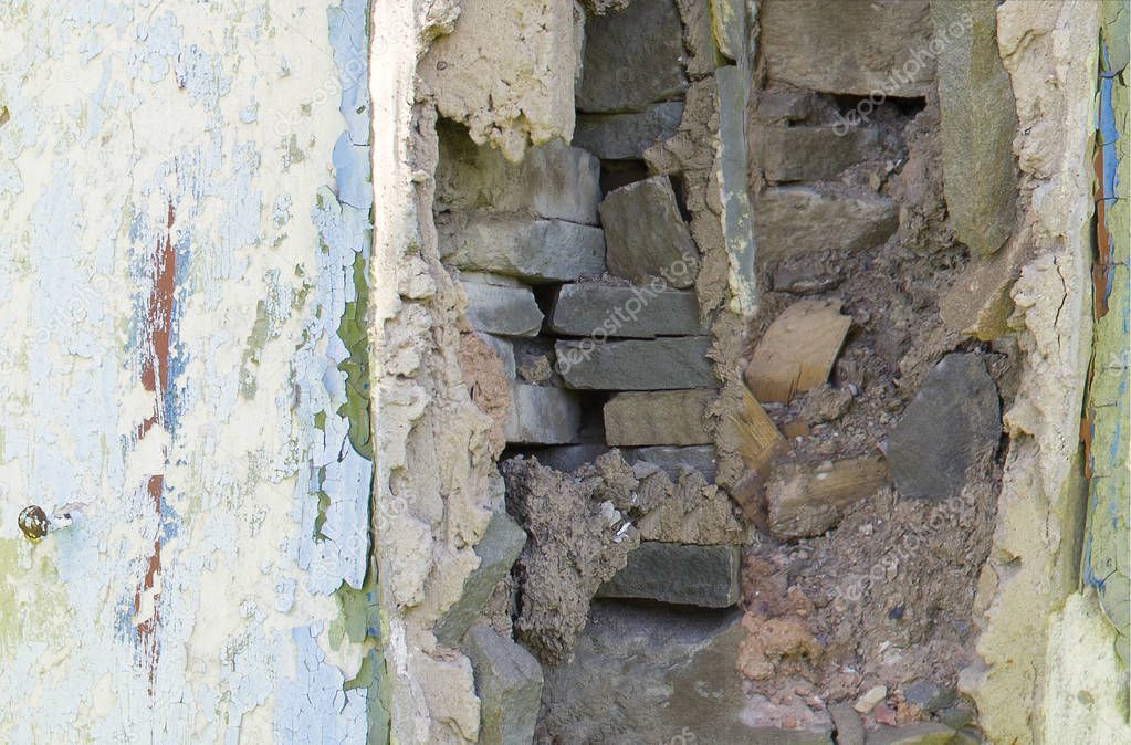 The window of the old abandoned house is lined with stones and clay. Against the background of a white wall of a dilapidated house