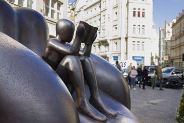 Prague. Czech. October 09, 2019. A metal sculpture of a boy sitting in an armchair and reading a book, covered with drops of autumn rain, against the backdrop of the city landscape.