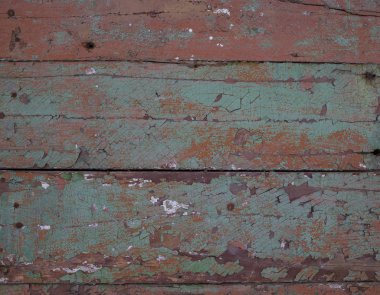 Doku. Kırık kırmızı, kahverengi ve yeşil boyalarla kaplı eski ahşap bir duvarın parçası. Yakın plan..