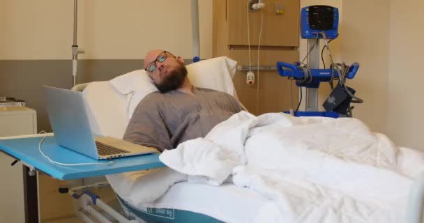 Βαριέται άνθρωπος περιμένει στο κρεβάτι του νοσοκομείου, χρησιμοποιώντας τον υπολογιστή του i νοσοκομείο, μονάδα καρδιολογίας. Αυτός ο ασθενής περιμένει το γιατρό και τη νοσοκόμα.. — Αρχείο Βίντεο