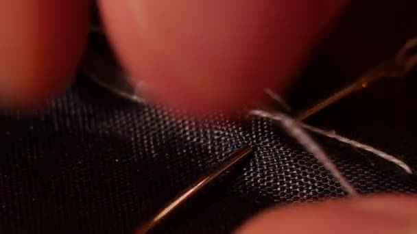 男性の巨視的なショットは白の自慢の糸で黒い線を縫い手を調整します。鋳造は、ミシンまたは手で、長い、簡単に取り外し可能なランニングステッチを縫製しています。タッキングとも呼ばれる。. — ストック動画