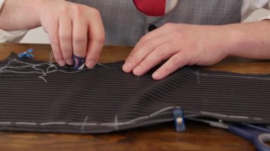 Tanınmayan bir adam terzinin elleri, kumaş parçalarını üst düzey İngiliz kumaşından bir ceketle diker. Bu terzilik işlemi koyu gri / siyah çizgili yün kumaş üzerinde yapılır..