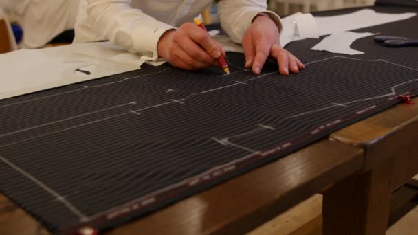 Χέρια του ανδρικού σχεδίου ράφτη στο στούντιο. το χέρι του ανθρώπου αντλεί με κιμωλία γεωμετρία σε μάλλινο ύφασμα. Αυτός ο σχεδιαστής για τα ρούχα και ράφτης καλλιτέχνης που εργάζονται για την παραδοσιακή μόδα — Αρχείο Βίντεο