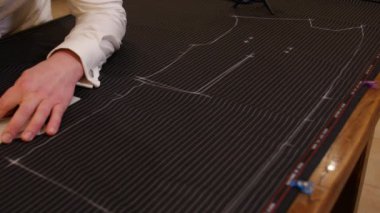 Ciddi terzi elleri ahşap masaya inanılmaz bir atölyeyle bir takım elbisenin desenini çiziyor. Stüdyoda çalışan genç çekici moda tasarımcısı