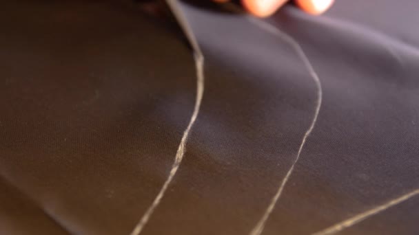 Un sarto sta tagliando le linee su un tessuto di seta acetato fodera con il suo gesso al fine di fare un abito — Video Stock