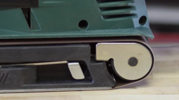 écologique Ponceuse à courroie électrique, ponceuse à main masculine. Traitement de la pièce sur une table en bois marron clair. Vue latérale, concept de recyclage du bois 