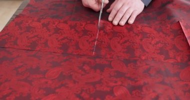 Moda tasarımcısı stüdyoda kırmızı desenli kumaşla terzilik aletleriyle çalışıyor. Desen, makas, mezura ve dikiş makinesi eskiz çizgilerindeki elbise detaylarını kesiyor.