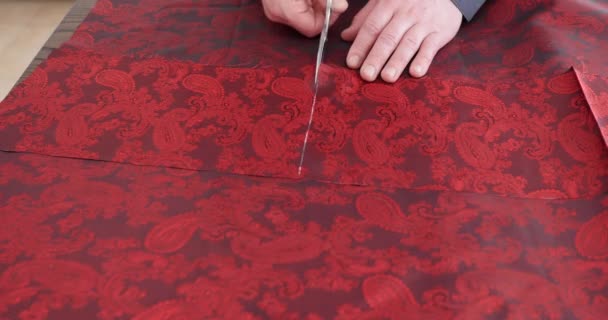 Créateur de mode travaillant avec du tissu de doublure paisley rouge au studio avec des outils de couture. Motif, ciseaux, ruban à mesurer, et une machine à coudre.. tailleur coupe détail de robe sur les lignes de croquis — Video