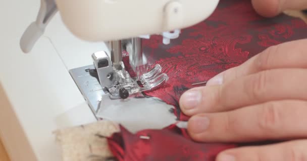 Handsome Male empuja el material de forro paisley rojo a través de una máquina de coser durante el proceso de fabricación del traje. Moda, creación y sastrería. Vista de ángulo alto — Vídeos de Stock