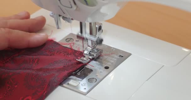 Close-up van de naaimachinenaald in beweging: de naald beweegt snel op en neer. De kleermaker naait rode paisley voerstof in de naaiatelier. Het proces van het maken van pakken. — Stockvideo