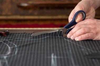 Dükkanında çalışan terzi, üzerine tebeşirle yaptığı elbisenin desenini işaretlediği ince çizgili siyah yün bir rulo kesiyor.