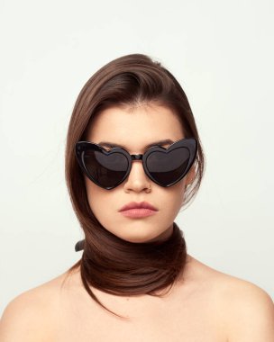 Moda gözlüklü kahverengi saçlı güzel bir kız beyaz bir arka planda çıplak omuzlarla poz veriyor, mesaj için boş bir alan.