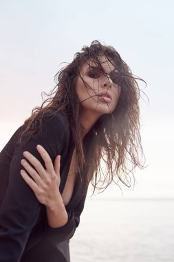 Güzel, genç ve atletik bir kız. Plajda siyah bir takım elbise giymiş. Gün batımı, yaşam tarzı ve moda.