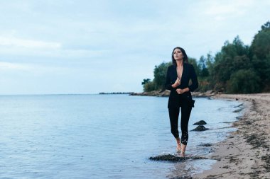 Sahilde yürüyen zarif bir kızın doğal fotoğrafı, doğal ışık altında moda seansı.