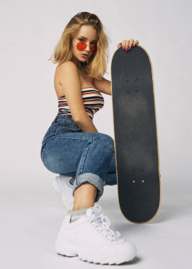 Kotlu ve kısa tişörtlü genç ve atletik bir kız, güzel ve sağlıklı bir ten, doğal sarı saç, boş arka plan, hassas makyaj