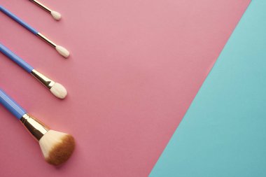 Pembe-mavi arka planda fırçalar ve makyaj süngerleri.,