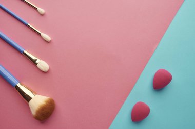 Pembe-mavi arka planda fırçalar ve makyaj süngerleri.,