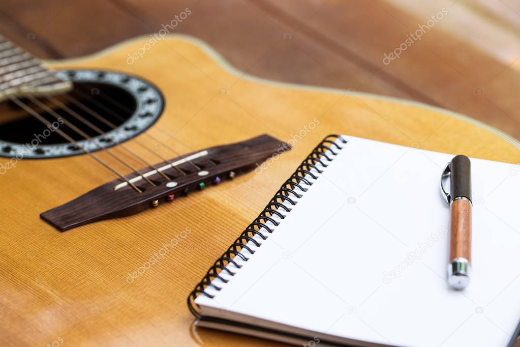 acoustic guitar with notebook and pen on wood background