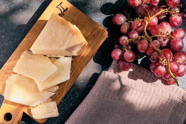 Pieces of parmigiano reggiano or parmesan cheese on wood board on dark background