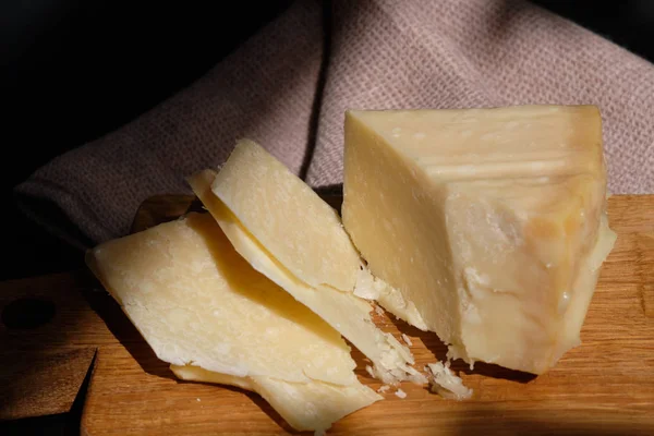 Pedaços de queijo parmigiano reggiano ou parmesão sobre tábua de madeira sobre fundo escuro — Fotografia de Stock