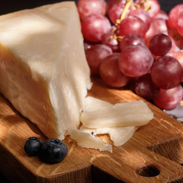Cijfers van parmigiano reggiano of parmezaanse kaas op houten plaat op donkere ondergrond — Stockfoto